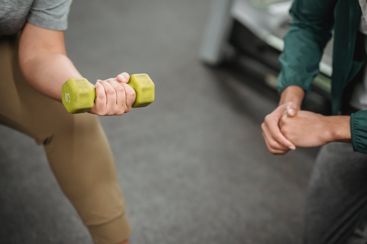 about-01 From above of crop anonymous instructor controlling female working out with dumbbell on blurred background of gym