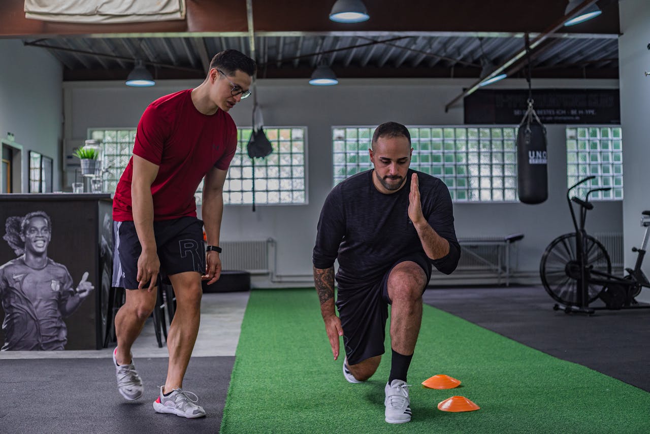 services-01 Full body of focused man in sportswear doing stretching exercises with coach in contemporary fitness center